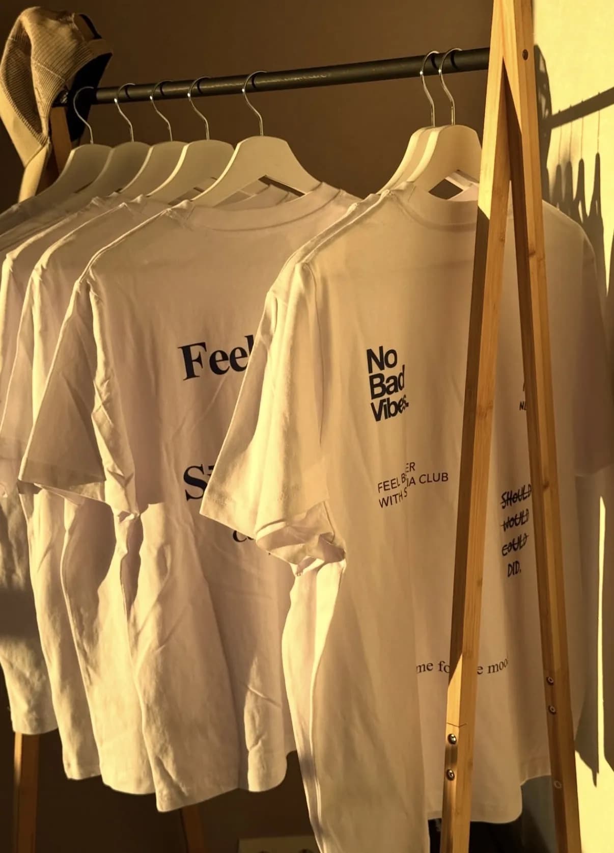 Tee-shirts blancs Sūana suspendus à un portant en bois
