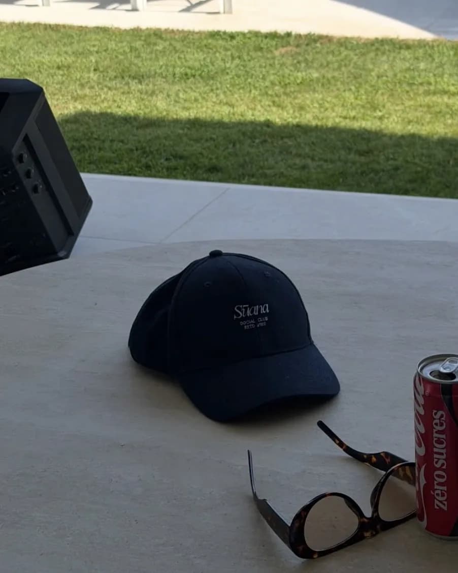Casquette bleu marine brodée du logo Sūana, posée sur une table en terrasse